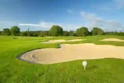Golf ball on a tee beside a sand bunker on a bright green fairway, representing Paul McGinley.