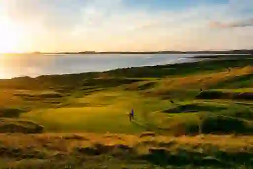 Golfer on a coastal links green at sunset with sea views, representing Graeme McDowell.