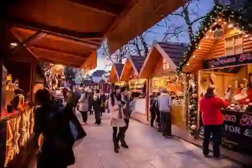 People browsing festive wooden stalls decorated with lights at Belfast Christmas Market.