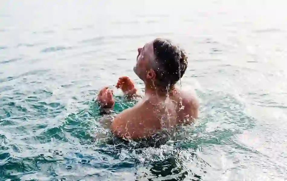 Man swimming in open water with head tilted back and droplets splashing from face and arms.