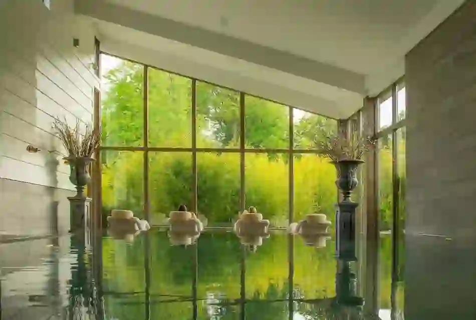 Bright spa lounge with tall windows, cushioned chairs and garden view framed by large vases.