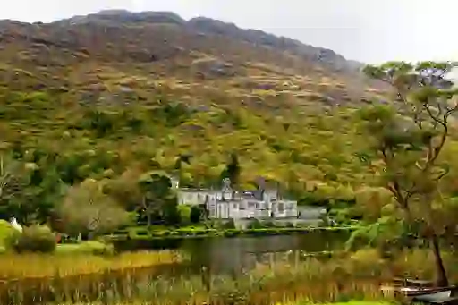 Gothic abbey beside a reflective lake, framed by lush forested mountain slopes.