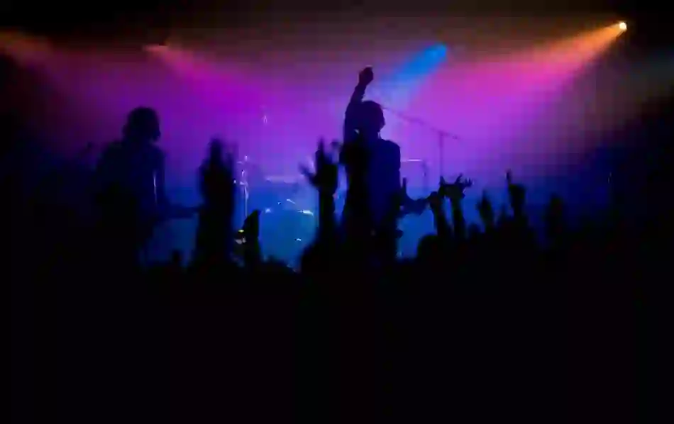 Concert crowd in Belfast with silhouettes of musicians on stage against purple and orange lights.