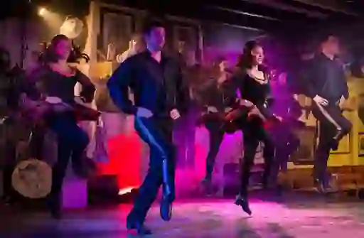 Irish dance troupe in black and red costumes perform on stage with purple lighting at Johnnie Fox's pub in County Dublin.