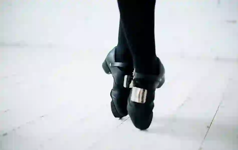 Close-up of Irish dancing shoes with metal taps worn by a dancer on a wooden floor.