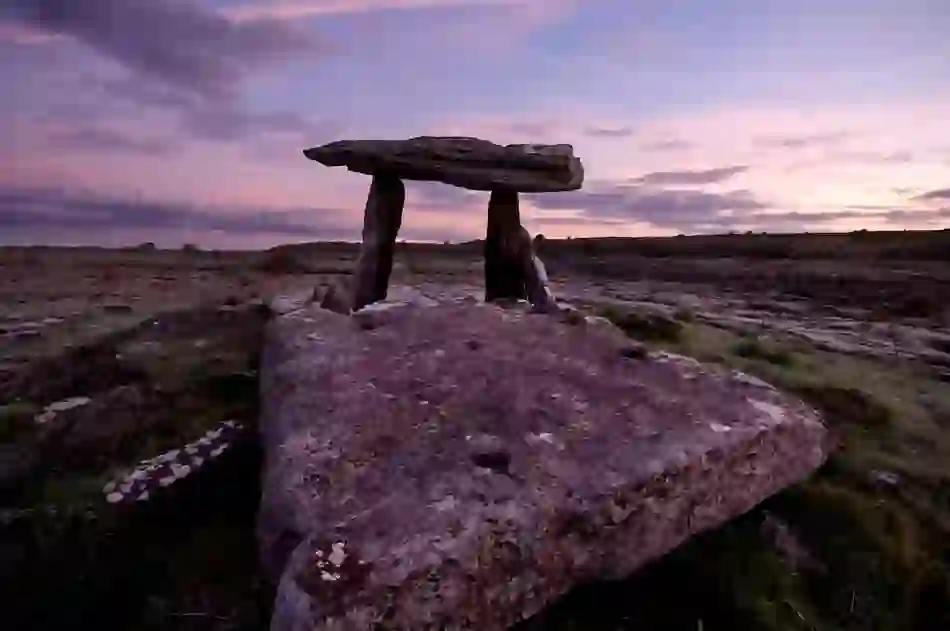 Karst limestone slabs of Poulnabrone Dolmen in the Burren, County Clare, at dusk with a purple sky overhead.