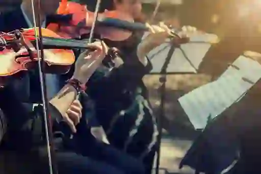 Close-up of musicians playing violins outdoors with sheet music stands.