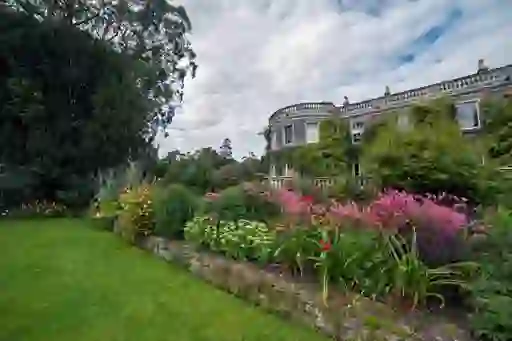 Historic Mount Stewart house with ivy-covered walls and vibrant flowerbeds under a cloudy summer sky.