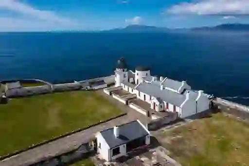White Clare Island lighthouse and cottages by the sea, with mountains visible in the distance.