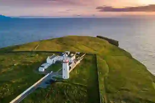 Loop Head lighthouse and cottages on grassy headland overlooking the Atlantic at sunset.