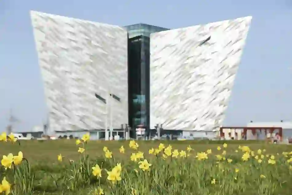 Titanic Belfast’s iconic ship-shaped building framed by daffodils under a bright spring sky.