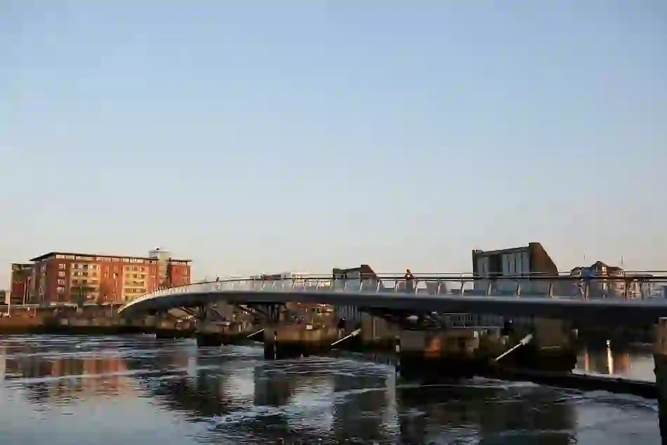 Lagan Bridge in Belfast spans the river, reflecting city buildings in the water at golden hour.