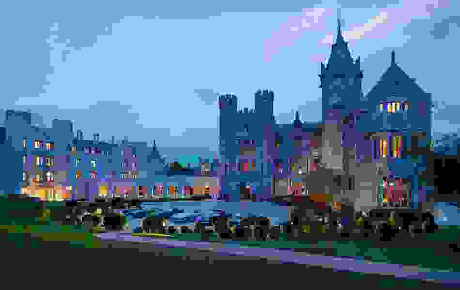 Luxury Adare Manor hotel in Ireland lit up at dusk with manicured gardens and elegant architecture.