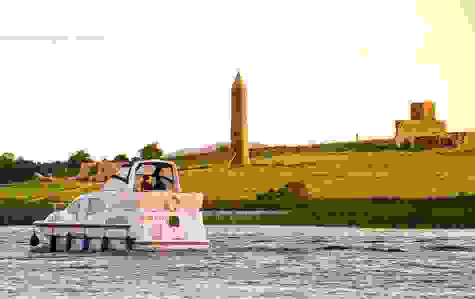 Boat cruising past historic round tower and ruins Devenish Island, County Fermanagh at sunset.