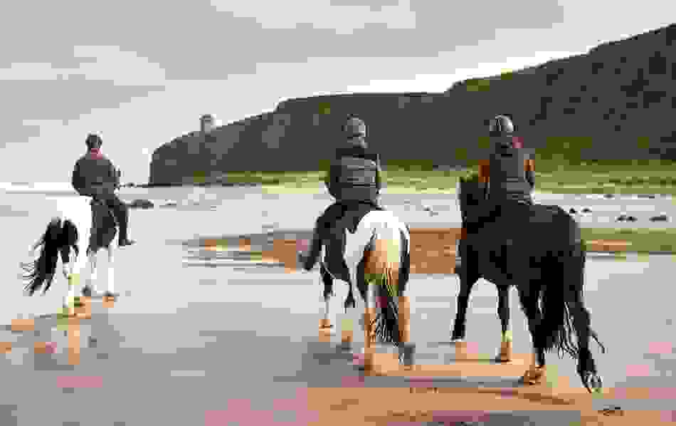 Horse riding on a sandy Irish beach with dramatic cliffs and Mussenden Temple in the background.