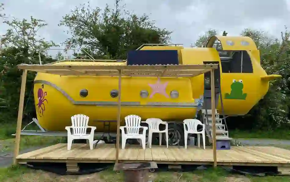 Yellow submarine-themed glamping pod with cartoon sea creatures and plastic chairs in County Monaghan.