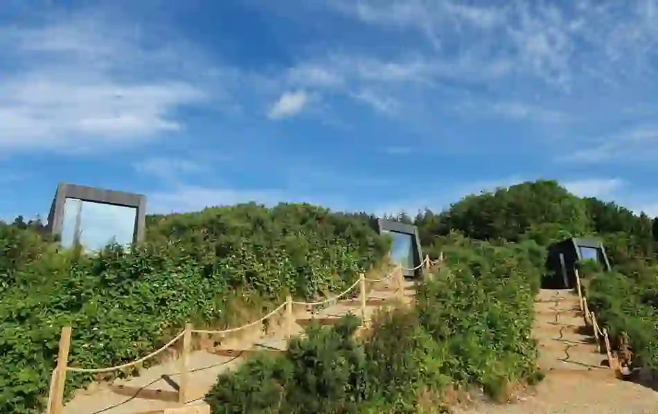 Tara Hill Estate glamping cabins with mirrored glass set into green shrubland under a bright blue sky in Wexford.