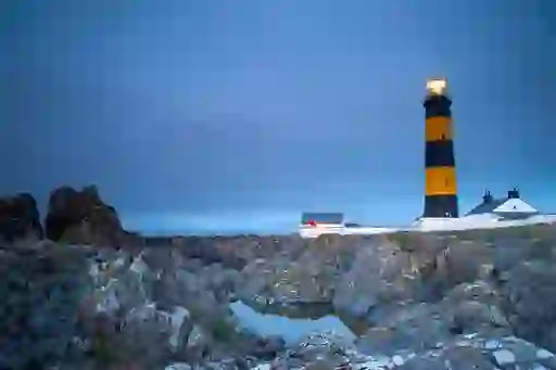 Black and yellow St John's Point Lighthouse with cottages on rocky shoreline at dusk in County Down.