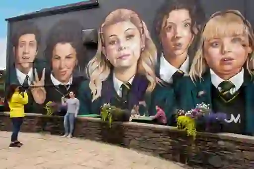Tourists pose for photos in front of the colourful Derry Girls mural on a gable wall in Derry~Londonderry.