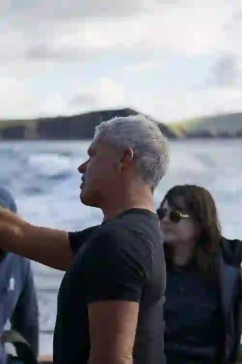 Male marine wildlife guide with short grey hair points toward the horizon while speaking to tourists on a boat off Dingle.