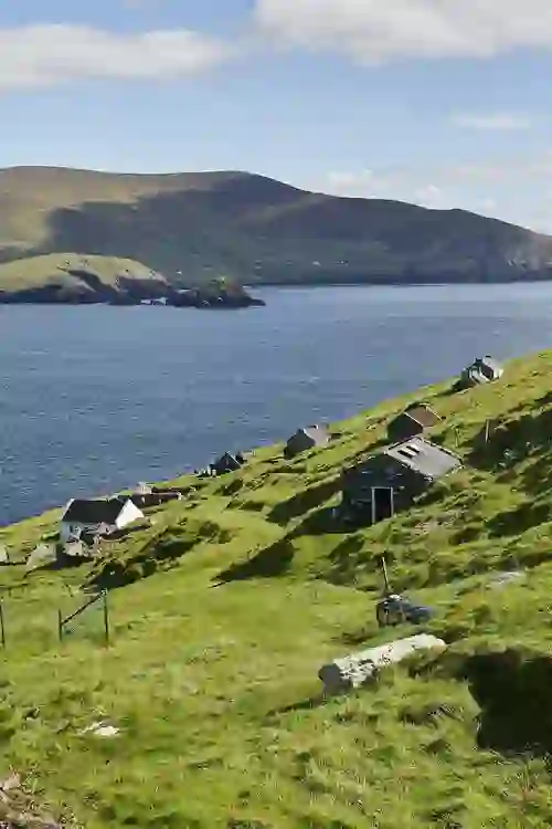 Row of old cottages along the hills of Great Blasket Island overlooking the sea, with the Kerry coast visible.