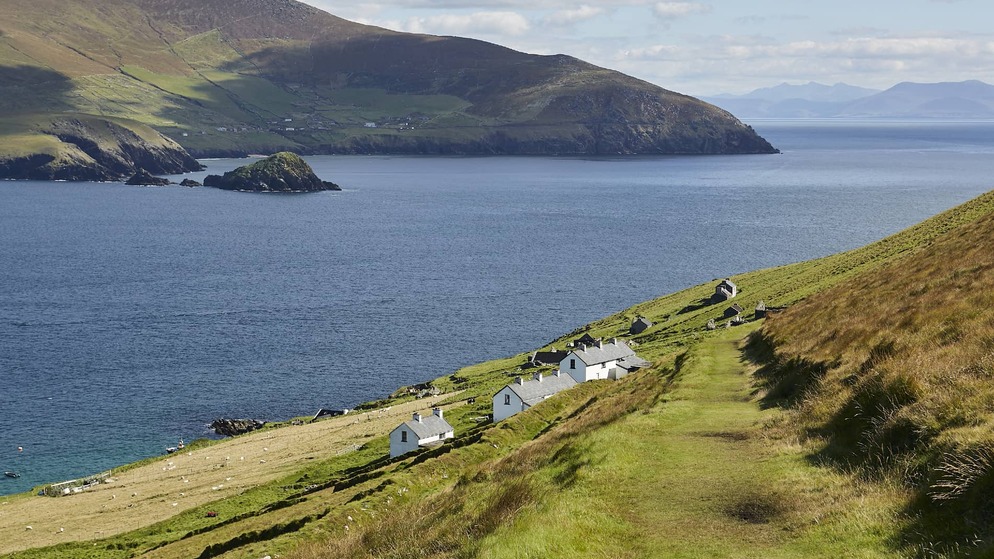 View of the Blasket Islands and mainland Kerry, with stone cottages dotting the hillside and calm Atlantic waters below.