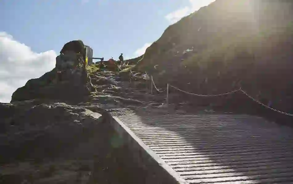 Steep landing and path leading up from the shore of Blasket Island, with sun flare above cliffs and safety chains in view.