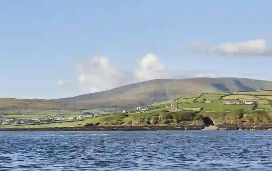 View of Ballydavid village with scattered houses and a medieval tower against the Slieve Mish mountains under a clear sky.