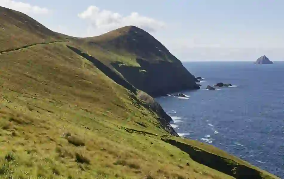 Sheer cliffs and grassy slopes of Great Blasket Island descending into the sea, with an island visible on the horizon.