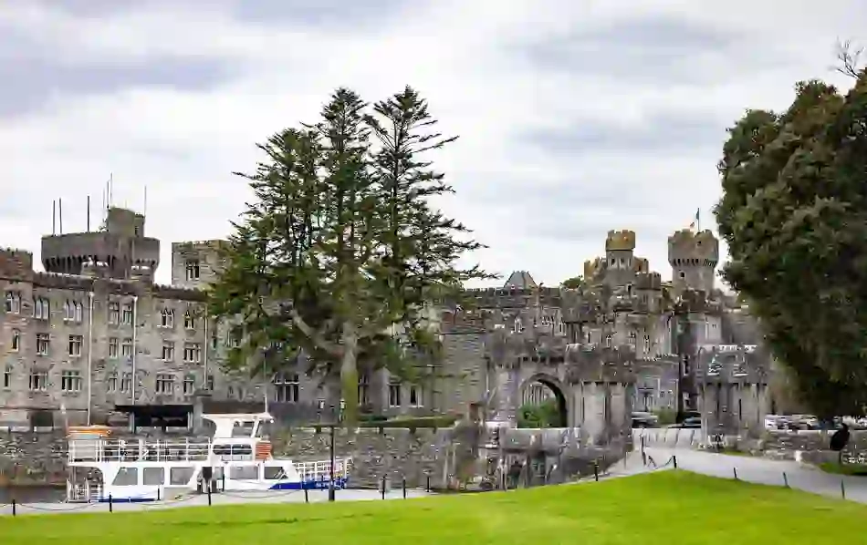 A sightseeing boat moored on the River Cong outside the grand stone façade of Ashford Castle.