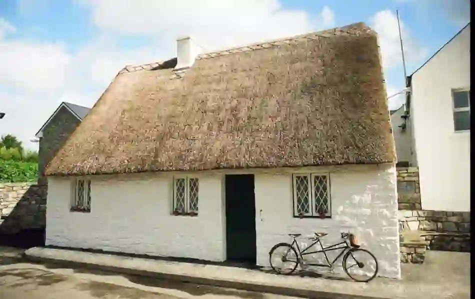 A traditional whitewashed thatched cottage with a black bicycle outside in a Mayo village near Cong.