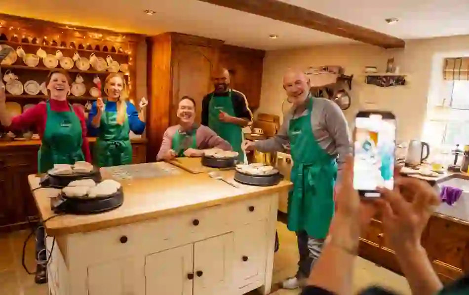 Smiling participants pose in aprons while cooking soda bread during a hands-on class in a warmly decorated kitchen.