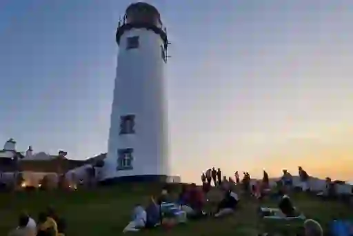 People relax on the grass beside Fanad Lighthouse in Donegal during Earagail Arts Festival at sunset.