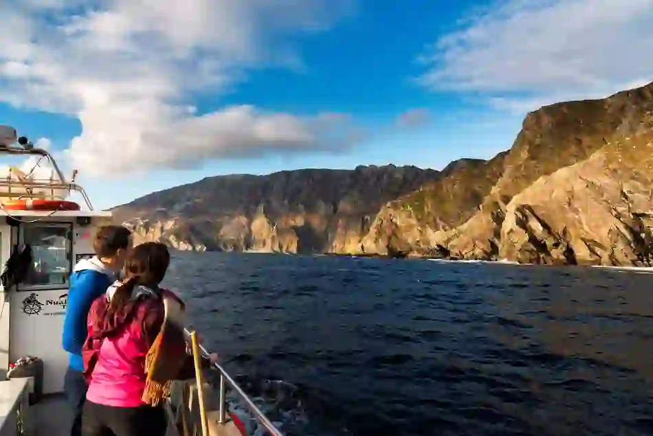 Two people on a boat admire the sea cliffs of Slieve League, rising steeply from the Atlantic in Donegal.