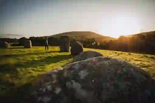 Person walking among granite boulders at Athgreany stone circle in Wicklow, with golden evening sun behind hills.