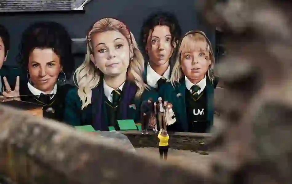 Tourists pose in front of the Derry Girls mural, showing five schoolgirls in uniform on Orchard Street.