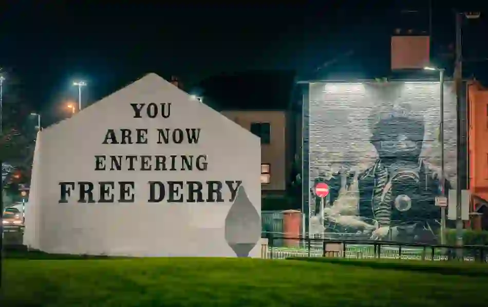 Illuminated Free Derry Corner sign and peace mural in the Bogside area of Derry at night.