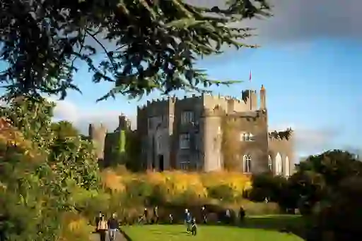Visitors strolling the gardens outside Birr Castle in County Offaly, framed by autumn trees and dramatic Gothic turrets.