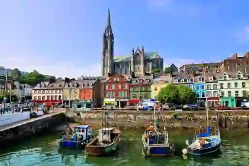 Fishing boats docked at the colourful harbourfront in Cobh, County Cork, with St Colman’s Cathedral towering above.
