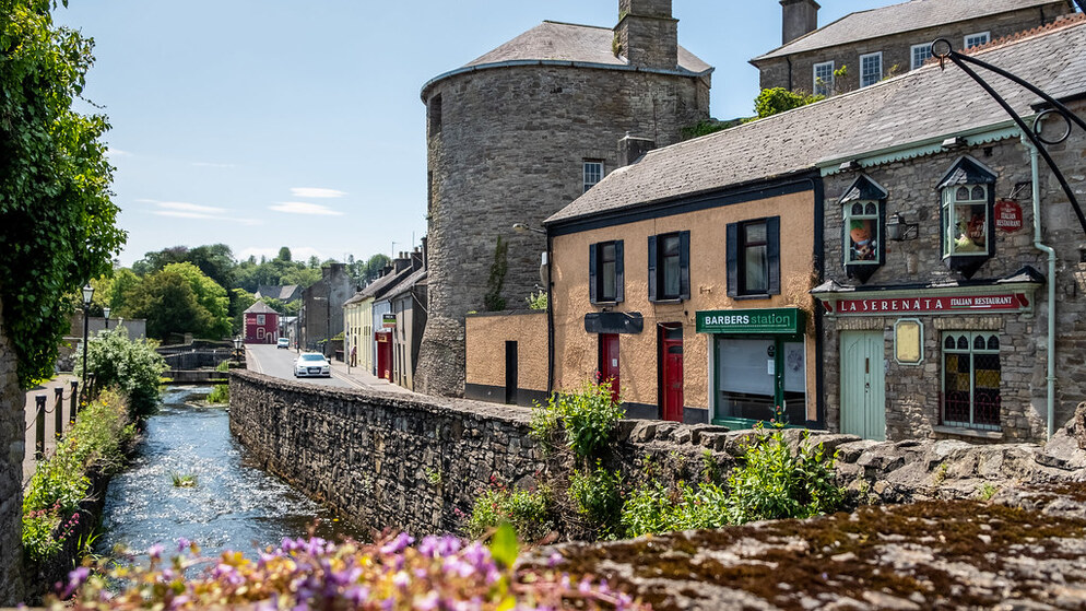 Historic round tower and riverside shops in Ireland on a sunny summer day.