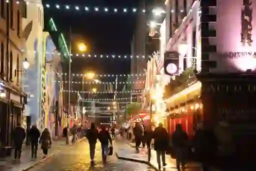 People walking under strings of lights along a lively Temple Bar street at night.