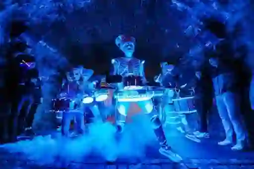 Costumed street performers playing illuminated drums during a Derry Halloween night event in a stone archway.