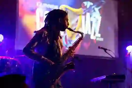 Saxophonist performing on stage at Cork Jazz Festival, with colourful lighting and a festival screen behind him.