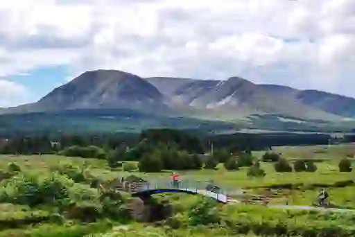 Cyclists crossing a bridge on the Great Western Greenway in County Mayo, with green fields and mountains beyond.