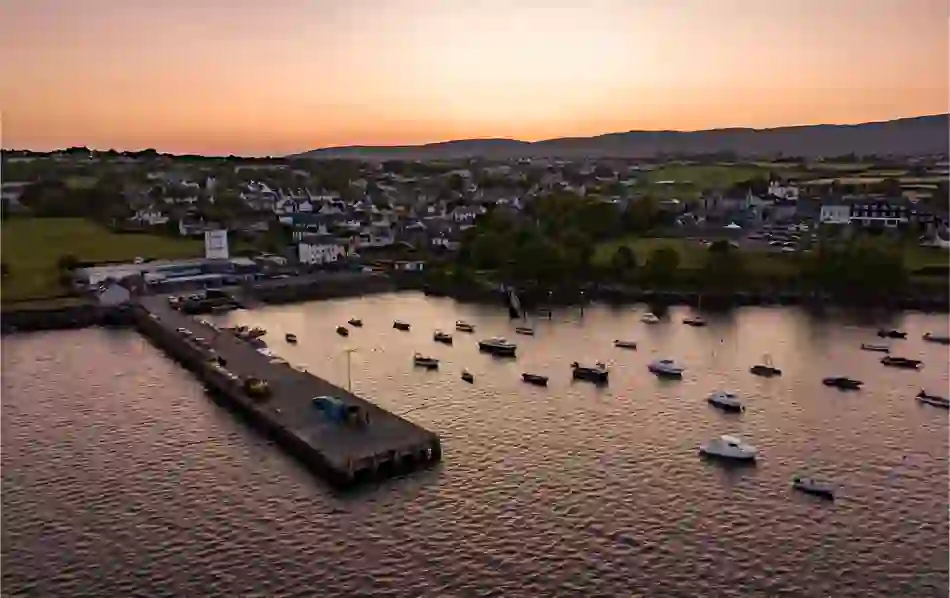 Sunset view over boats moored at Schull harbour in Cork with the town and hills in the background.