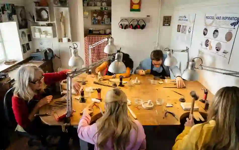 Group of people learning jewellery making around a workbench at Gobbins Craft studio.