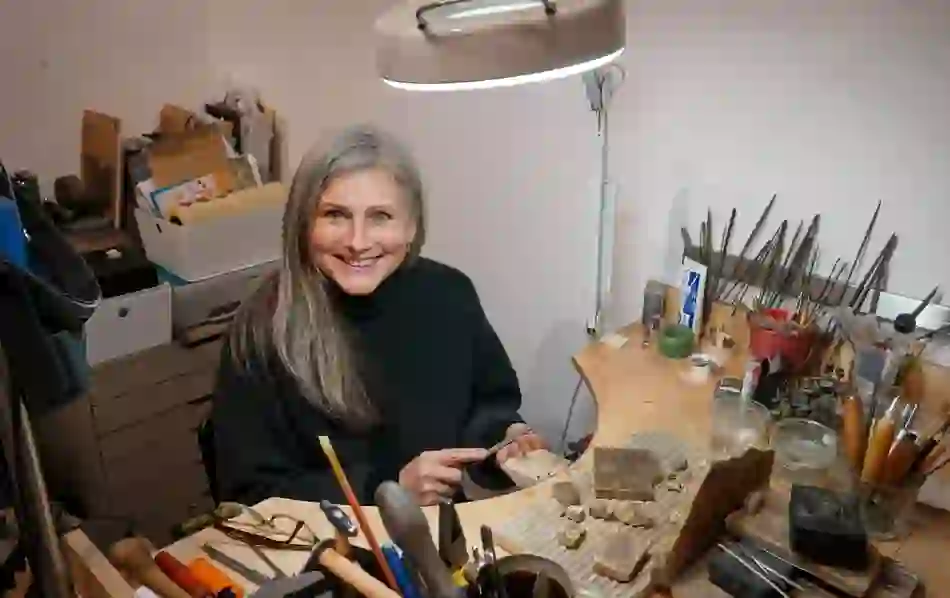 Smiling craftswoman working with stone and tools in her jewellery studio.