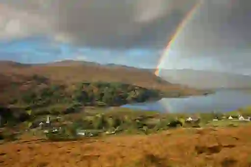 Rainbow arching over hills, a lake and scattered cottages in the scenic Dunlewey countryside, County Donegal.