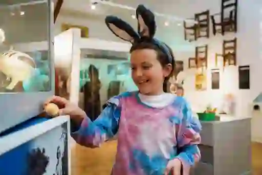 Smiling child wearing bunny ears headband during an Easter egg hunt in a brightly lit Tipperary Museum of Hidden History.