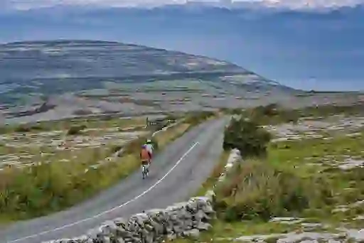 Two cyclists riding along a quiet road through the rocky limestone landscape of the Burren, County Clare.